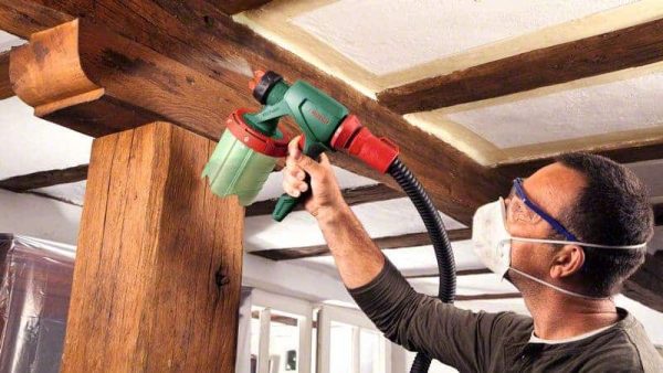 Čovjek s maskom i naočalama koristi Bosch PFS 3000-2 za prskanje boje na drvenom stupu.