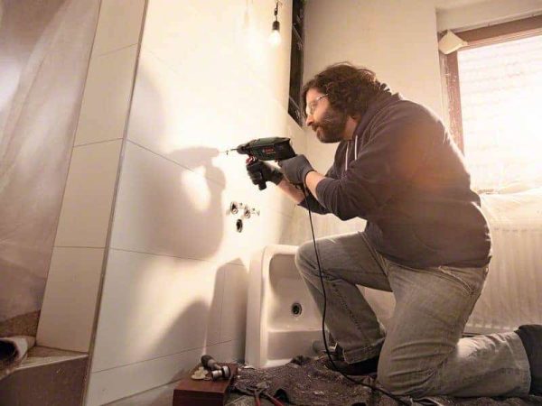 Muškarac s Bosch udarnom bušilicom UniversalImpact 700 buši zid u kupaonici.