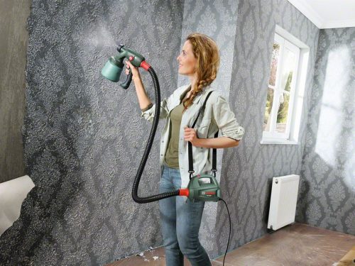 Žena s BOSCH PFS 2000 sustavom za prskanje boje u sobi s ukrasnim tapetama.