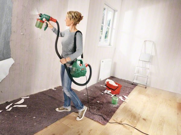Žena s Bosch PFS 3000-2 uređajem za prskanje boje na bijelom zidu u sobi.