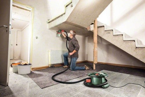 Muškarac s maskom i odjevnom odjećom čisti podove usisivačem u stanu.