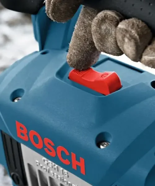 Ruka u rukavici pritiska crvenu sigurnosnu tipku na Bosch GSH 16-30 udarnom čekiću.