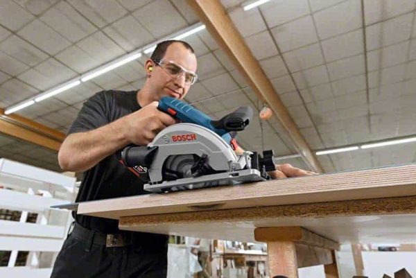 Muškarac koristi Bosch GKS 18V-57 G aku kružnu pilu na radnom stolu u radionici.