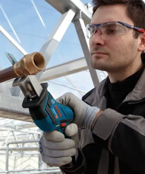 Muškarac s naočalama i zaštitnim naočalama koristi Bosch aku recipročnu pilu GSA 12V-14 za rezanje metala na gradilištu.