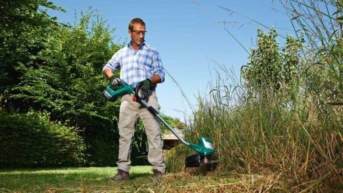 Muškarac s BOSCH AdvancedGrassCut 36 aku trimerom za travu u vrtu, obrezivanje visokog trnja i trave.