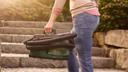 Žena drži Bosch EasyVac 3 ručni usisavač na otvorenom prostoru s kamenim stepenicama u pozadini.