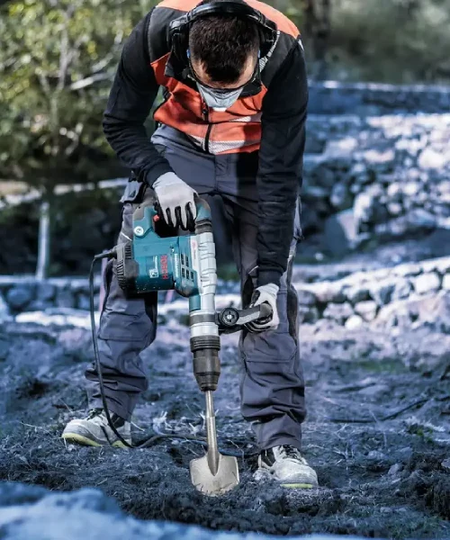 Muškarac koristi električnu bušilicu za iskopavanje na obali rijeke u prirodi.