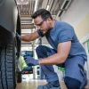 Muškarac s naočalama i zaštitnim slušalicama koristi Bosch aku udarni odvijač PRO GDS18V-450P na automobilu.