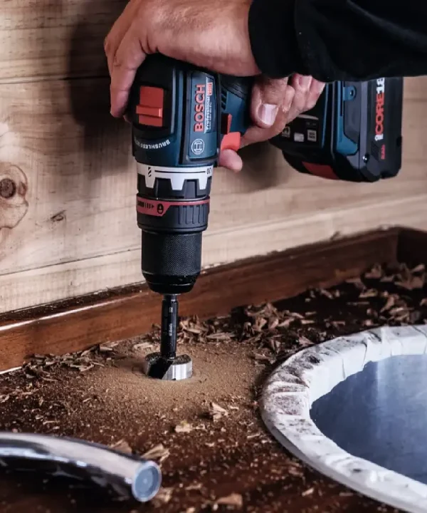 Bosch udarna bušilica s čekićem u ruci radi u vrtu pored materijala i cijevi.
