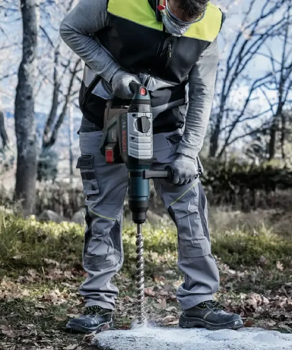 Radnik s bušilicom Bosch SDS-max izbušava kamen u vanjskom prostoru.