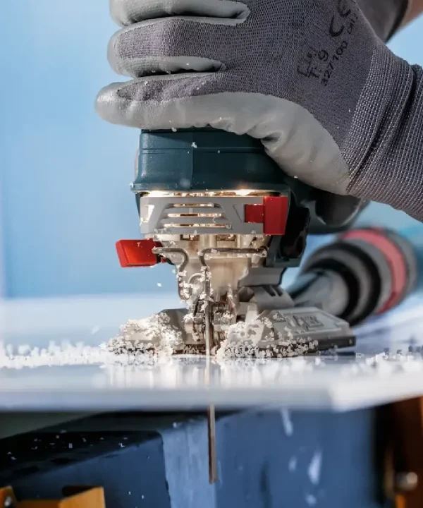 Ručna električna ubodna pila u upotrebi na plastičnom materijalu uz zaštitne rukavice.